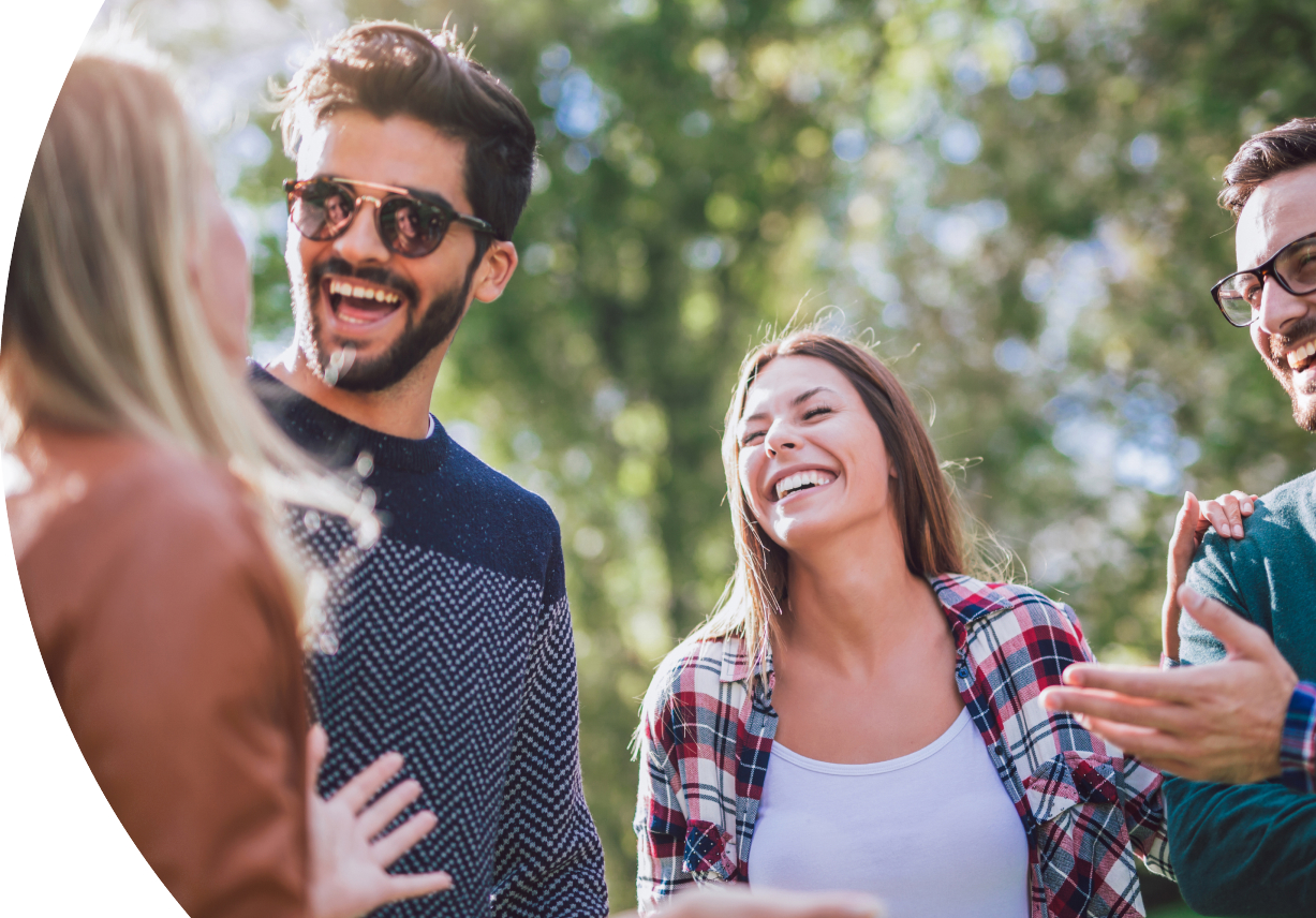 Two couples laughing together outdoors with trees in the background